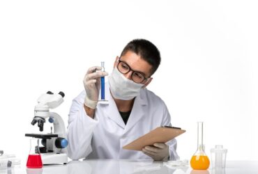 front-view-male-doctor-white-medical-suit-with-mask-due-covid-writing-notes-white-desk_140725-87382