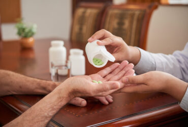Crop shot of doctor putting pills in hand of senior man sitting at table